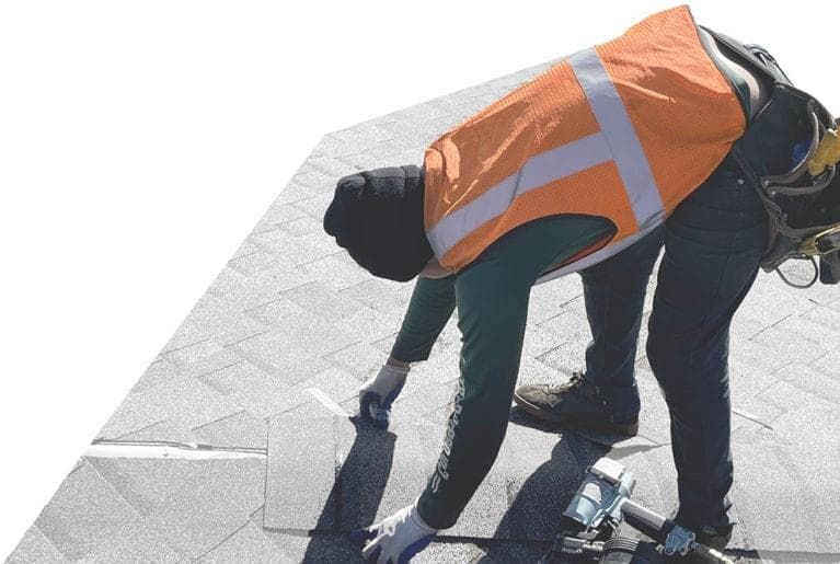 Metro City Roofing crew member in an orange vest bending over to install ridge cap in Denver, Colorado