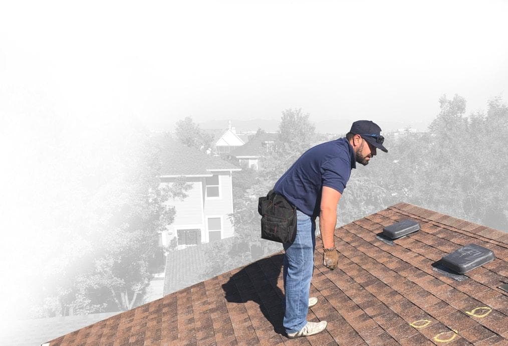 Metro City Roofing salesperson in a blue shirt and black hat inspecting a red shingle roof and marking hail impact marks in yellow chalk in Denver, Colorado with blue sky in the background
